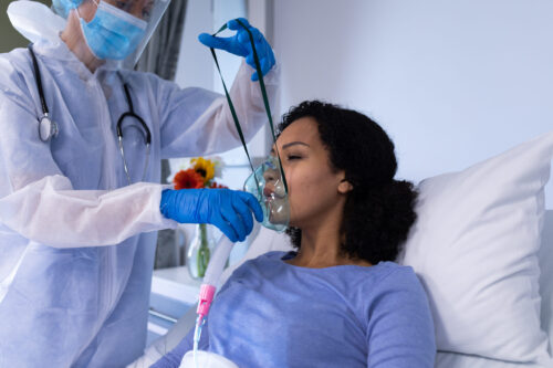 Caucasian female doctor in ppe suit putting ventilator on african american female patient. medicine, health and healthcare services during coronavirus covid 19 pandemic.